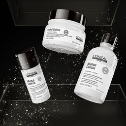 Three L'Oréal Professionnel Paris Metal Detox haircare products floating on a black background with spark effects: a white jar with a black lid, a white bottle with a black cap, and a white tube with a black cap. The products are labeled 'Metal Detox' and 'Série Expert'.