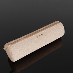 A rectangular, textured light beige pouch with a gold zipper and three small gold button details, resting on a reflective black surface.
