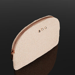 A small zippered pouch with a textured cream-colored top half and a dark brown bottom half, featuring a rose gold zipper and three small metal eyelets on the top edge, set against a dark reflective background.