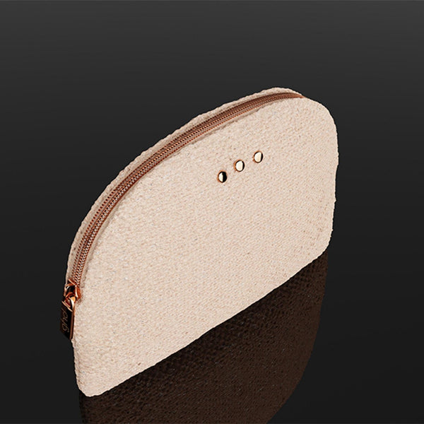 A small zippered pouch with a textured cream-colored top half and a dark brown bottom half, featuring a rose gold zipper and three small metal eyelets on the top edge, set against a dark reflective background.