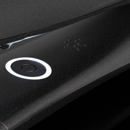 Close-up of a black textured electronic device featuring a circular white-lit power button and a small array of tactile button details.