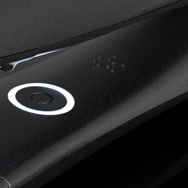 Close-up of a black textured electronic device featuring a circular white-lit power button and a small array of tactile button details.