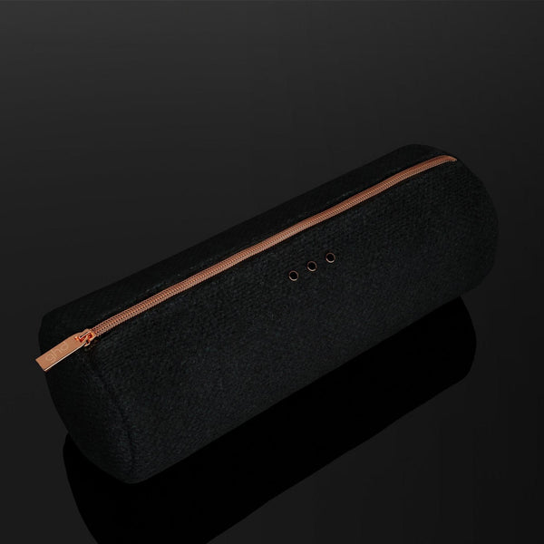 A black cylindrical fabric speaker or pouch with a metallic rose gold zipper and three small circular ports on top, shown on a reflective black background.