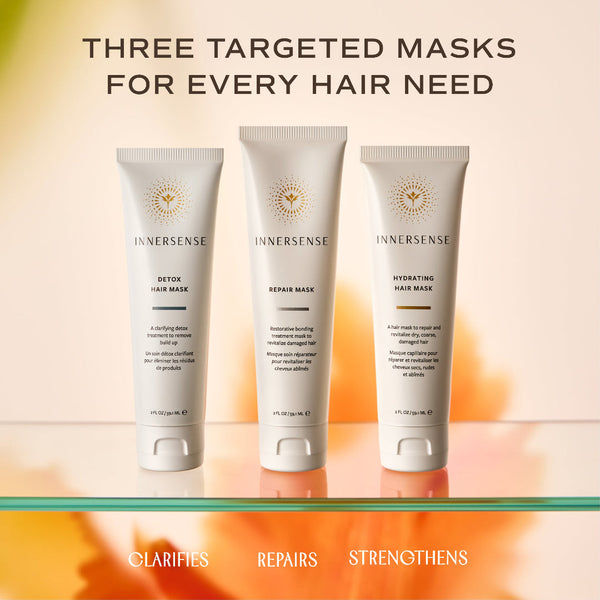 Three Innersense targeted hair masks in white squeeze tubes are displayed on a glass shelf against a warm beige and orange gradient background. The top text reads 'THREE TARGETED MASKS FOR EVERY HAIR NEED' and the bottom text lists the mask types: 'CLARIFIES', 'REPAIRS', and 'STRENGTHENS'.