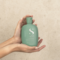 Hand holding a green bottle with a brand logo against a beige background