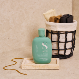 Green bottle with logo on a beige surface next to a woven basket with clothes.