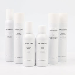 Six white cylindrical cosmetic bottles and cans from the brand SACHAJUAN, arranged in a row against a seamless white background.