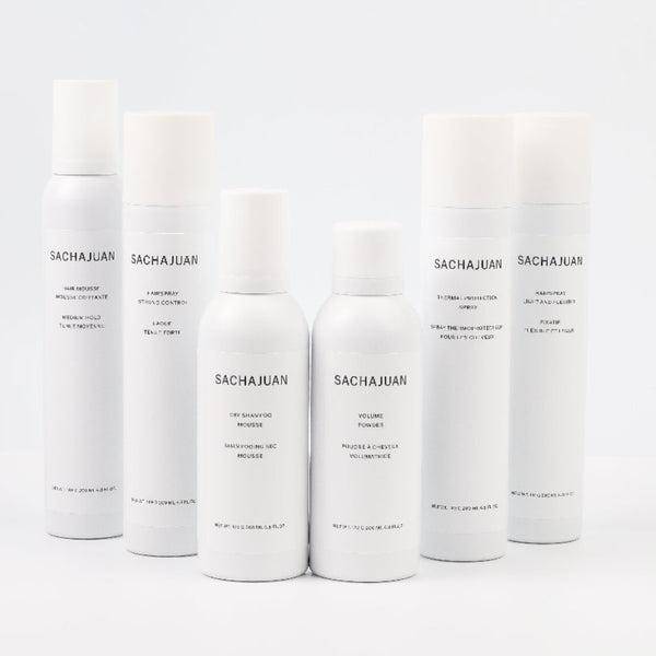 Six white cylindrical cosmetic bottles and cans from the brand SACHAJUAN, arranged in a row against a seamless white background.