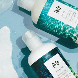 a close up of two R+Co Atlantis Moisturizing B5 Shampoo bottles