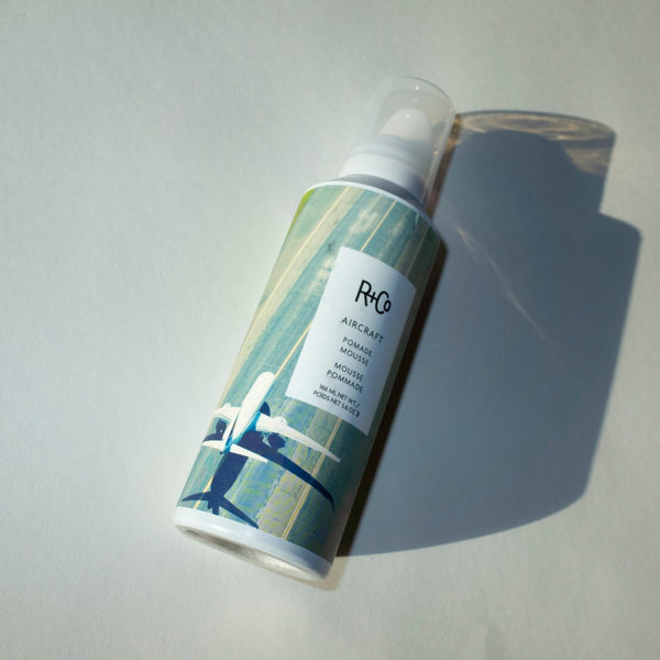 a closeup  of a R+Co Aircraft Pomade Mousse bottle