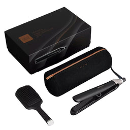A hair styling kit on a white background, including a black flat iron, a black paddle brush, a black cylindrical carrying case with a rose gold zipper, and a black presentation box.
