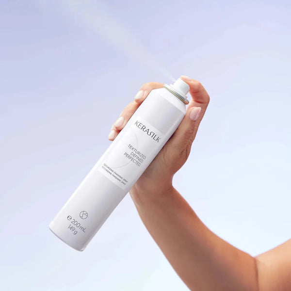 Hand holding a Kerastilik hair product bottle against a light purple background