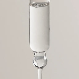 A clear glass dropper pipette containing a white liquid, shown vertically against a neutral light gray background.