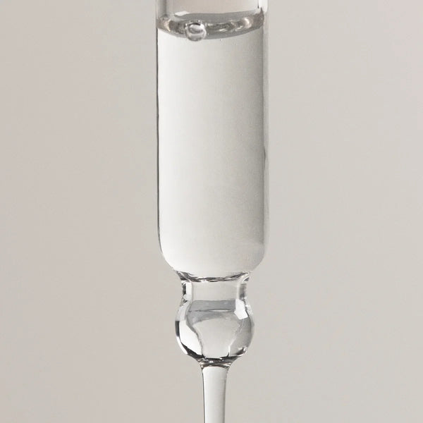 A clear glass dropper pipette containing a white liquid, shown vertically against a neutral light gray background.