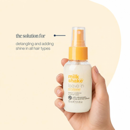 A hand holding a bottle of Milk Shake Leave In Conditioner against a warm beige background with promotional text on the left.