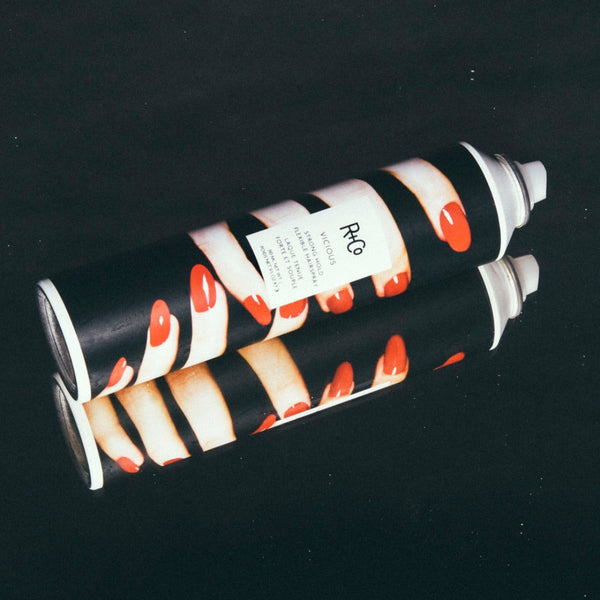 R+Co Vicious Strong Hold Flexible Spray on a dark reflective surface